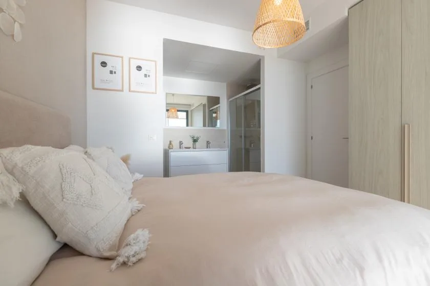 Un dormitorio con la cama tendida y un baño visible al fondo.