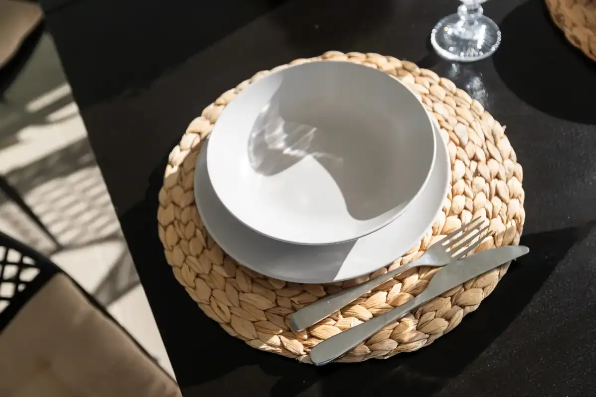 Un plato y un cuenco blancos están sobre un mantel individual tejido en una mesa oscura.