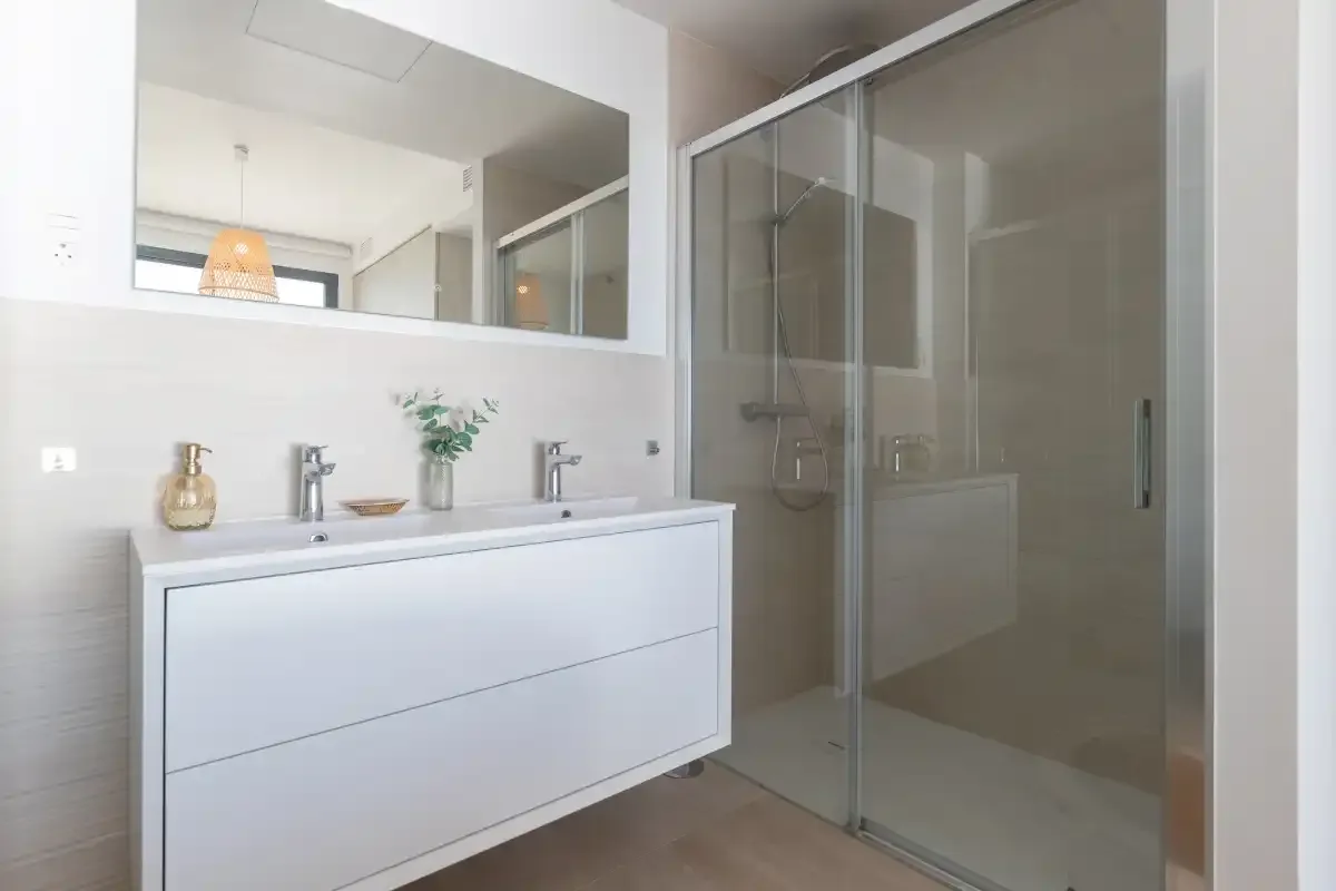Un baño luminoso con un lavabo blanco y una ducha de vidrio.
