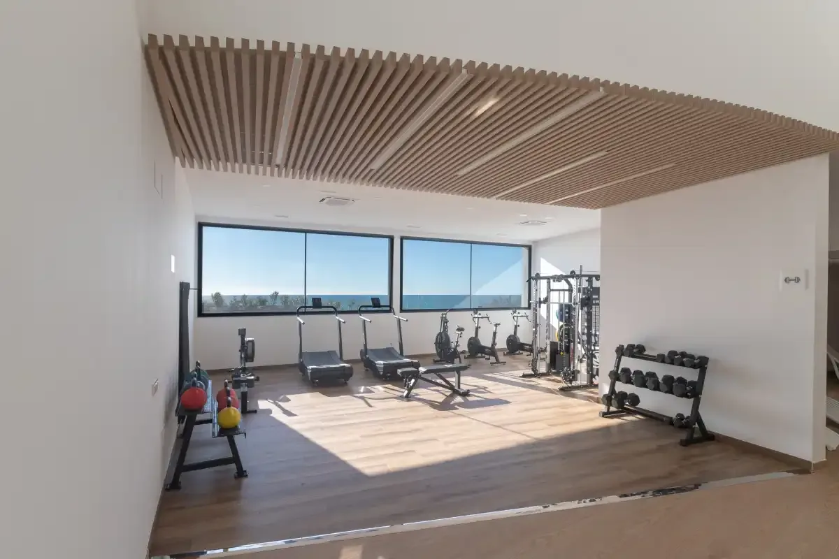 Una luminosa sala de fitness con máquinas de ejercicio y pesas junto a grandes ventanas.