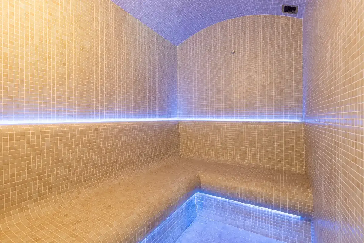 Un baño de vapor alicatado con un banco integrado e iluminación azul.