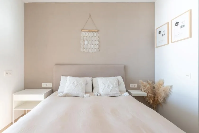 Un dormitorio con una cama bien tendida y un adorno colgante en la pared.