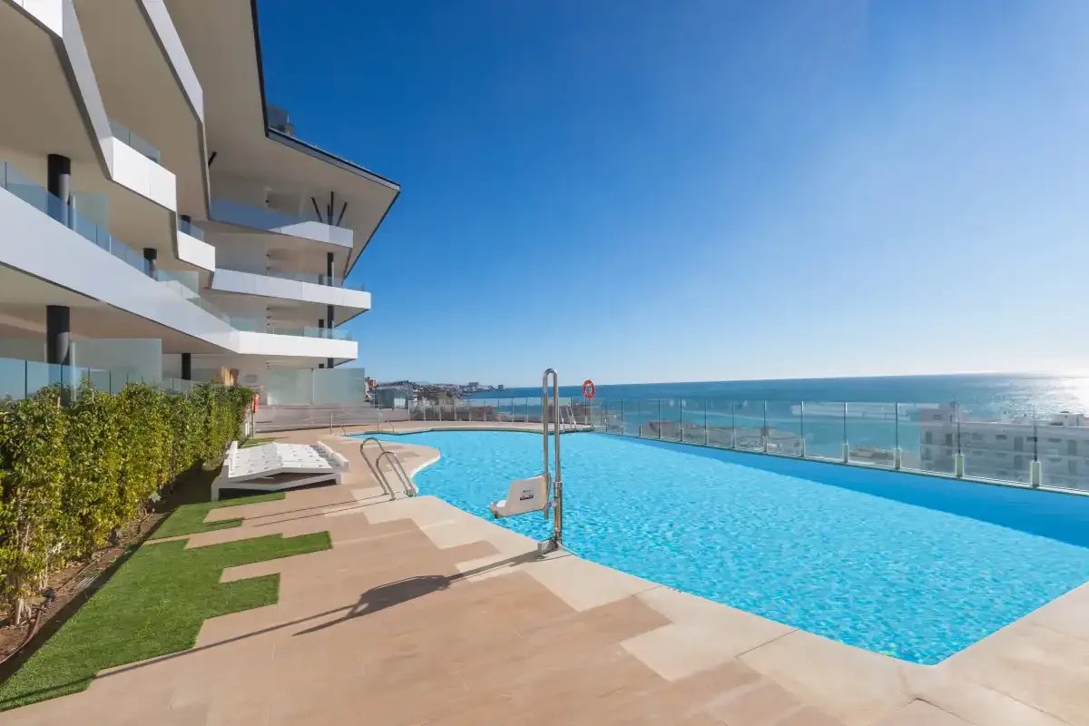Una piscina en la azotea junto a apartamentos modernos tiene vistas al mar.