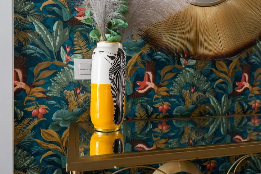 Un jarrón decorativo y una lámpara de mesa destacan sobre un papel pintado botánico colorido.