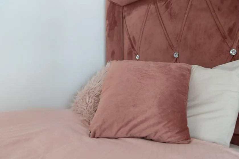 Una cama con ropa de cama rosa y almohadas frente a un cabecero tapizado.