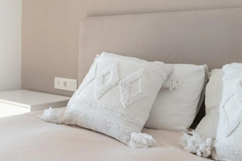 Una cama de dormitorio con almohadas blancas y cojines decorativos.