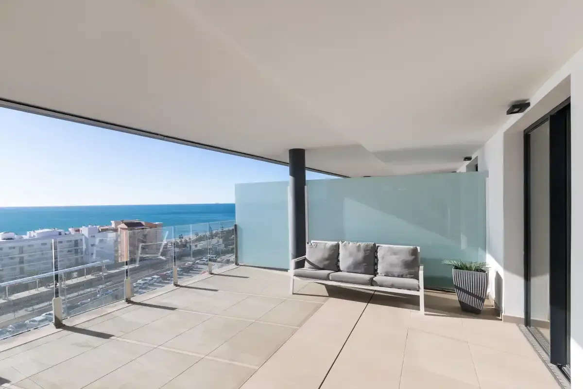 Una terraza con asientos y una barandilla de vidrio tiene vistas al mar.