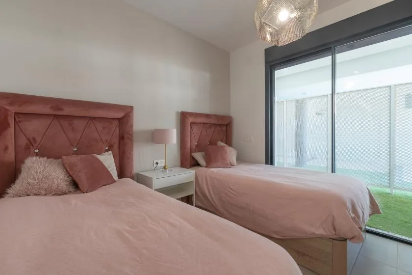 Un dormitorio con dos camas, ropa de cama rosa y una gran puerta corrediza de vidrio.