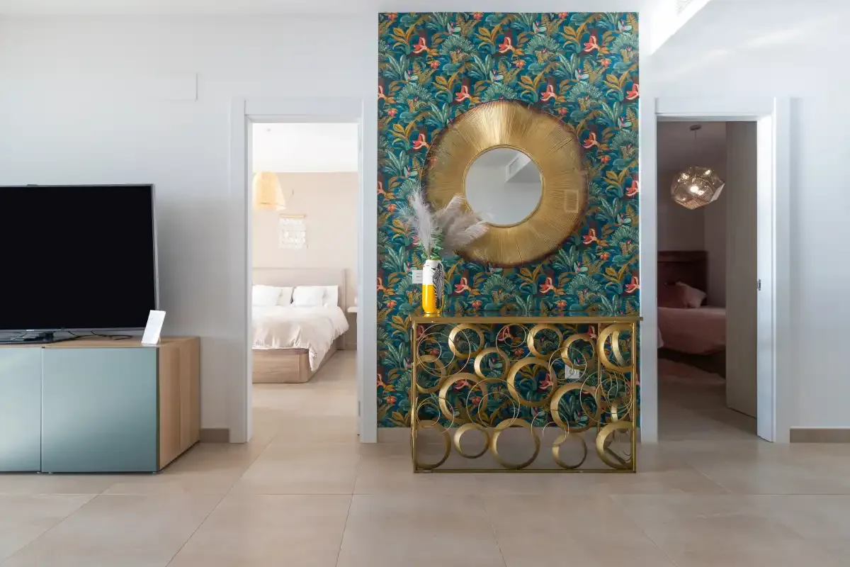 Una sala luminosa con un televisor y una consola decorativa frente a una pared estampada.