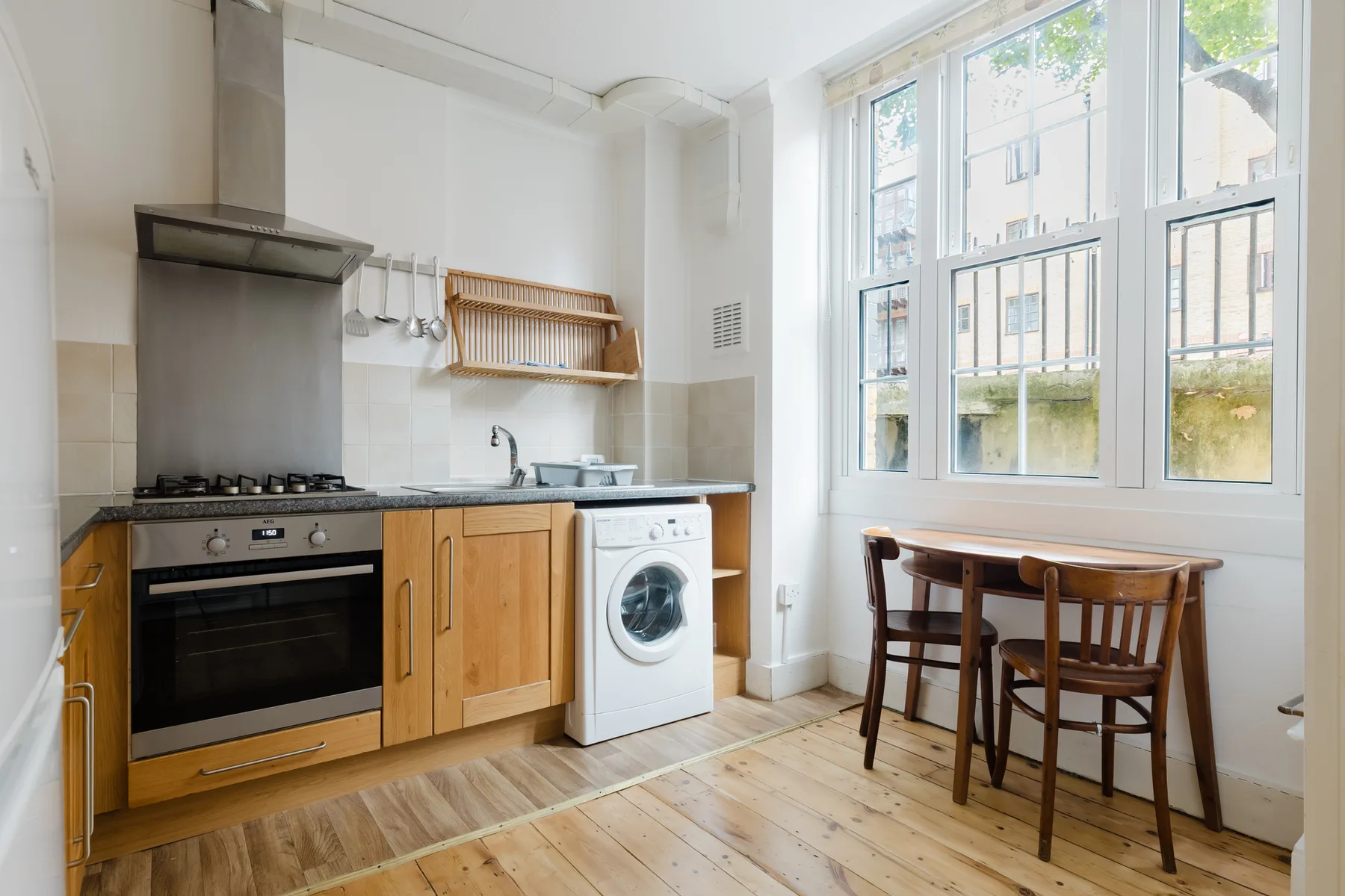 A bright kitchen with a stove, washing machine, and dining table by the windows.