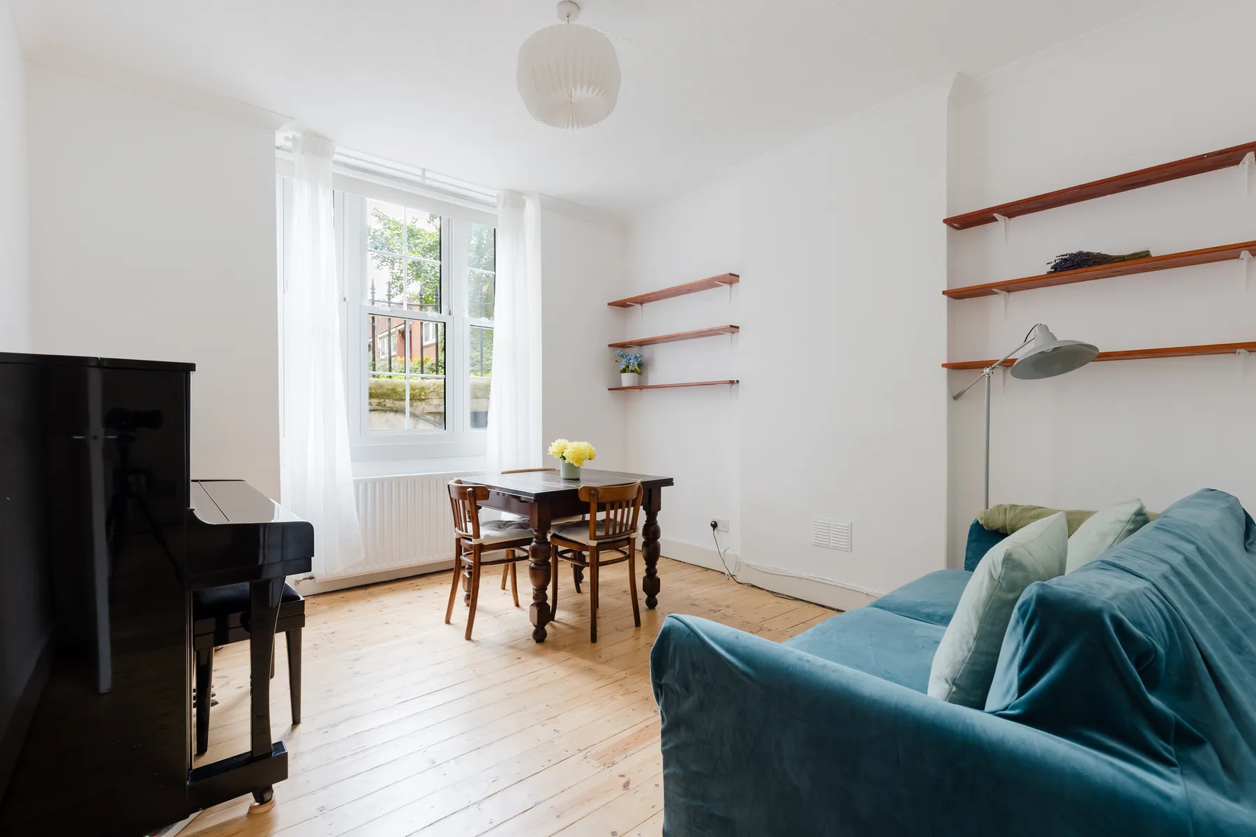 A bright living room with a piano, dining table, and blue seating.
