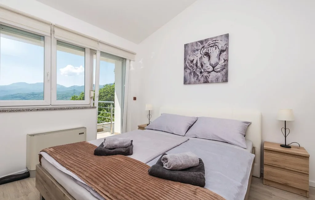 A bedroom with a bed and large windows overlooking a green landscape.