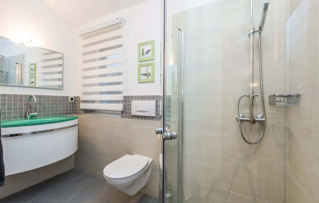 A modern bathroom with a glass shower, wall-mounted sink, and toilet.