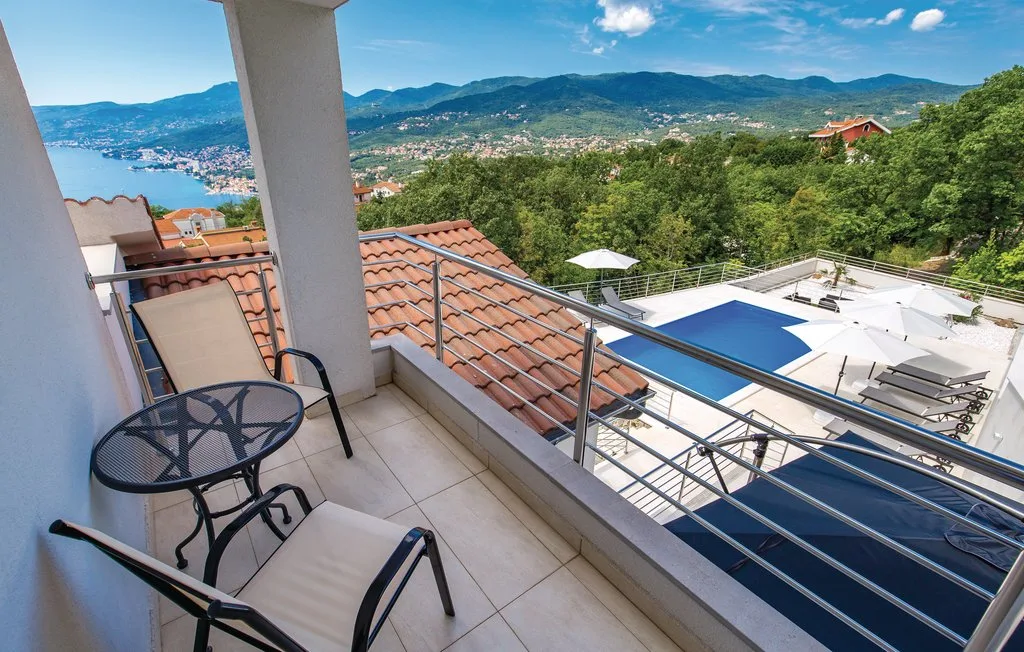 A balcony overlooks a swimming pool, wooded hills, and a distant bay.