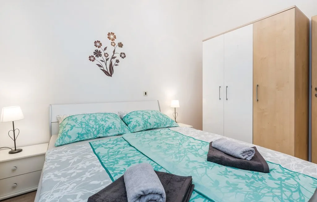 A bedroom with turquoise patterned bedding, bedside lamps, and a wardrobe.