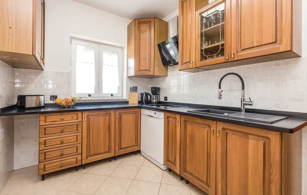 A kitchen with wooden cabinets, dark countertops, and a sink beneath the window.