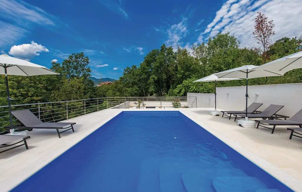 An outdoor swimming pool is surrounded by lounge seating and umbrellas.