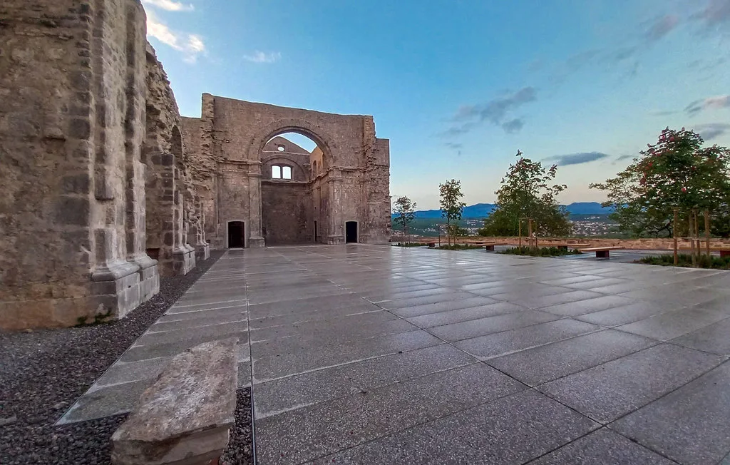 A broad paved terrace beside a historic stone building, with distant hills beyond.