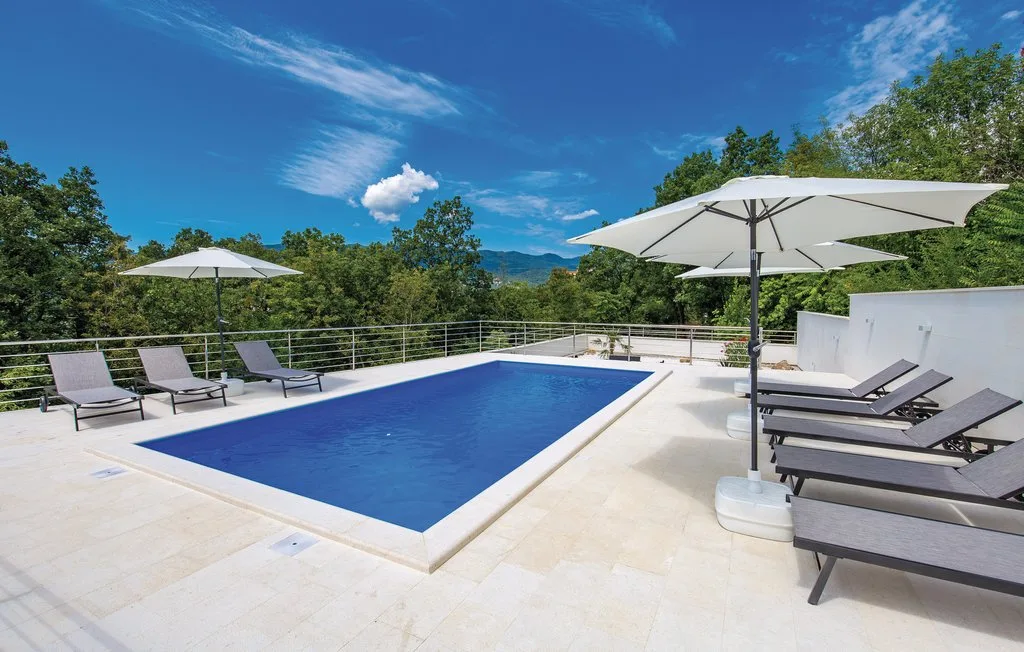An outdoor swimming pool is surrounded by loungers and patio umbrellas.