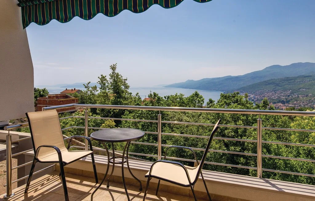 A balcony with seating overlooks a green valley and distant water.