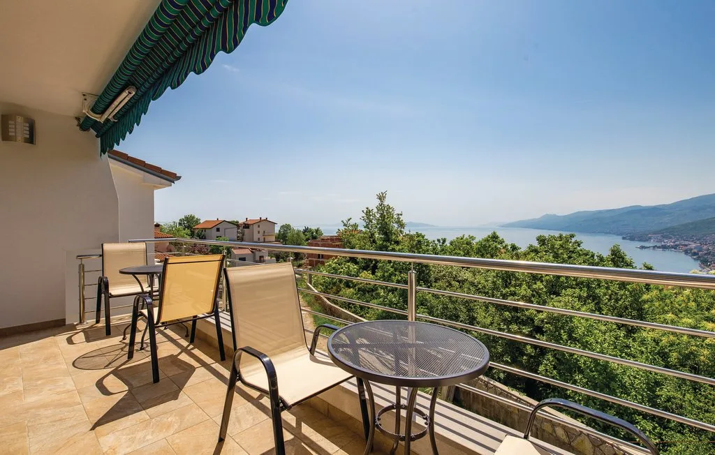 A tiled balcony overlooks green hills and a bay, with outdoor seating.
