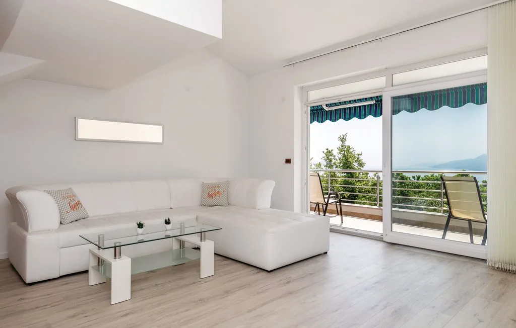 A bright living room with white seating, a glass coffee table, and large windows.