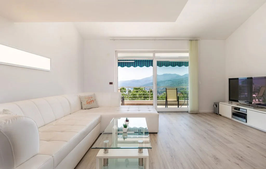 A bright living room with seating and a glass coffee table, opening onto a balcony.