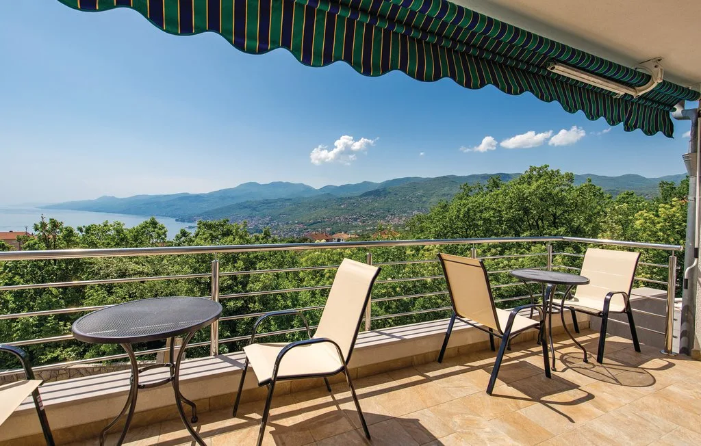 A terrace with outdoor seating overlooks green hills beneath a striped awning.