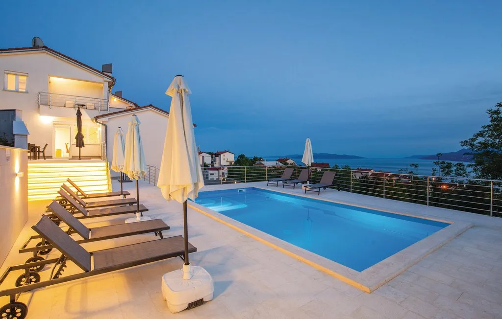 Outdoor pool beside lounge seating, with buildings and the sea visible beyond.