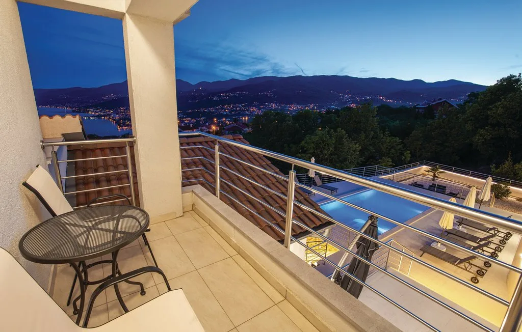 A balcony overlooks a lit pool and a mountain town at dusk.
