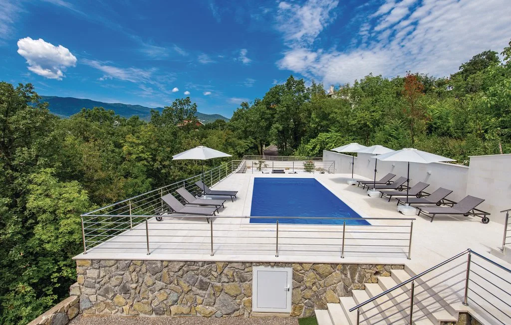 An outdoor swimming pool sits on a terrace surrounded by wooded hills.