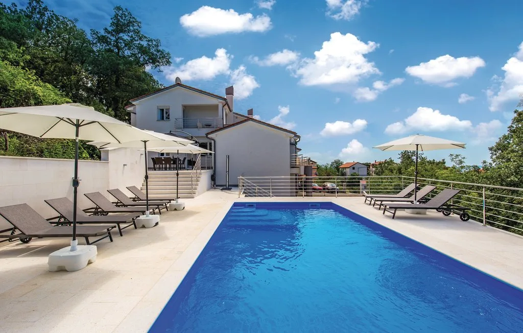 An outdoor swimming pool sits beside a house, with loungers and umbrellas on the patio.