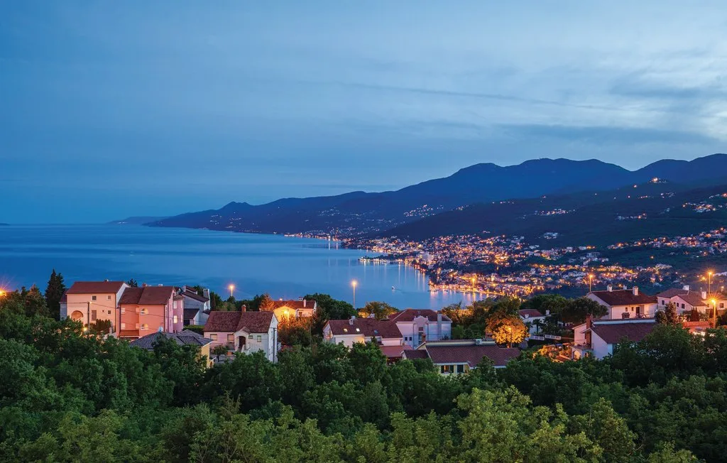 A coastal town at dusk overlooks a calm bay and surrounding mountains.