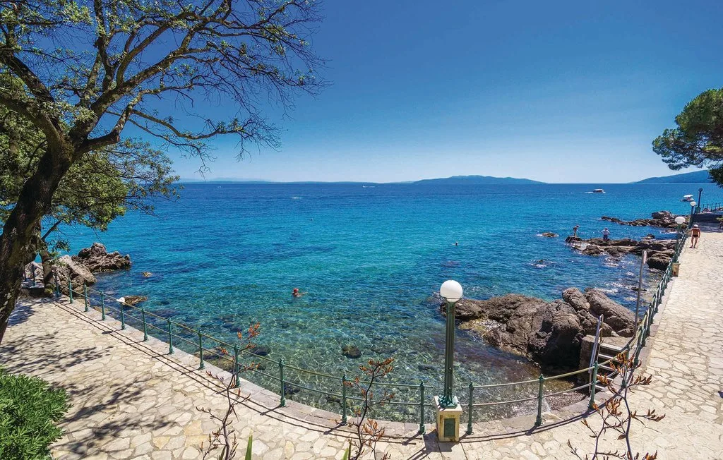 A seaside walkway follows the clear blue water beside a rocky shore.