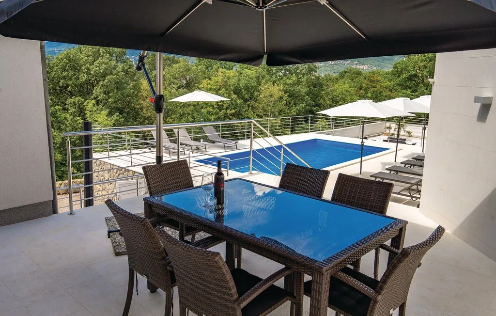 Outdoor dining table and seating overlook a swimming pool and green hillside.
