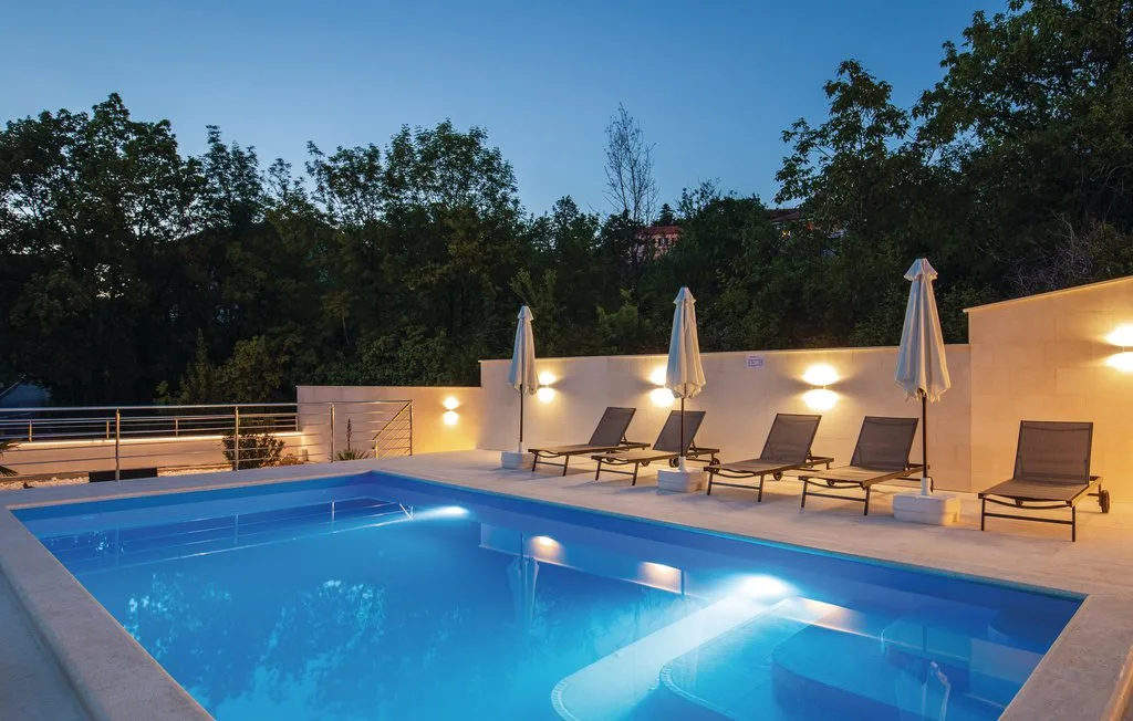 An outdoor swimming pool is surrounded by lounge seating and closed umbrellas.