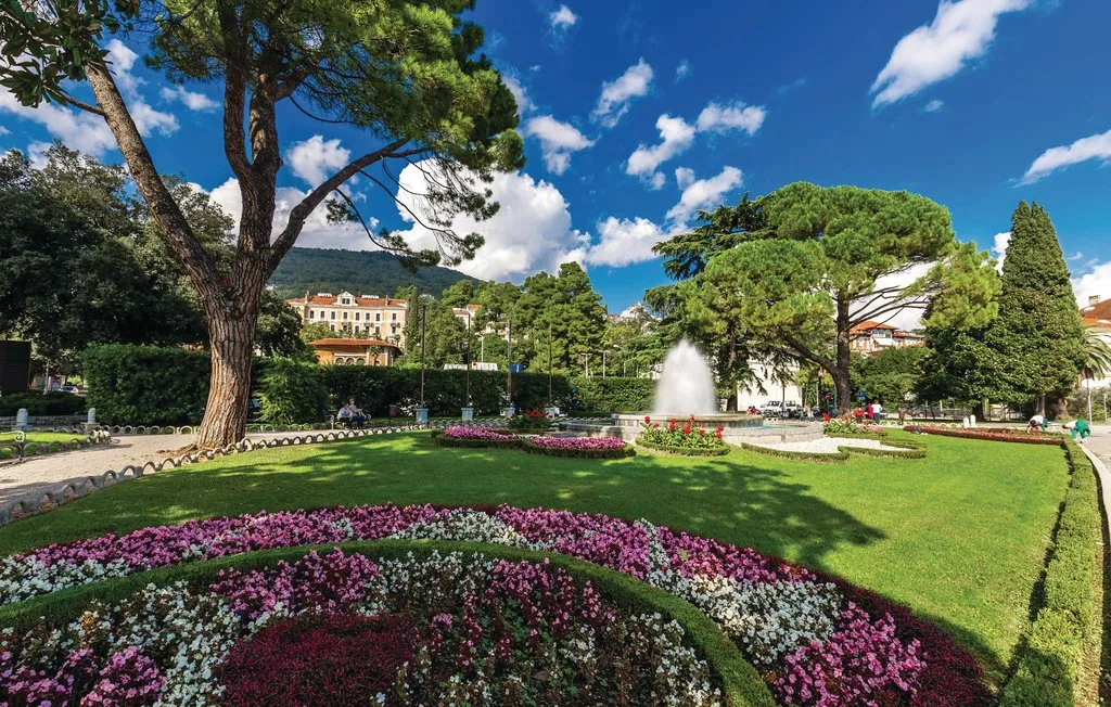 A landscaped garden with curved flower beds, lawns, trees, and a fountain.