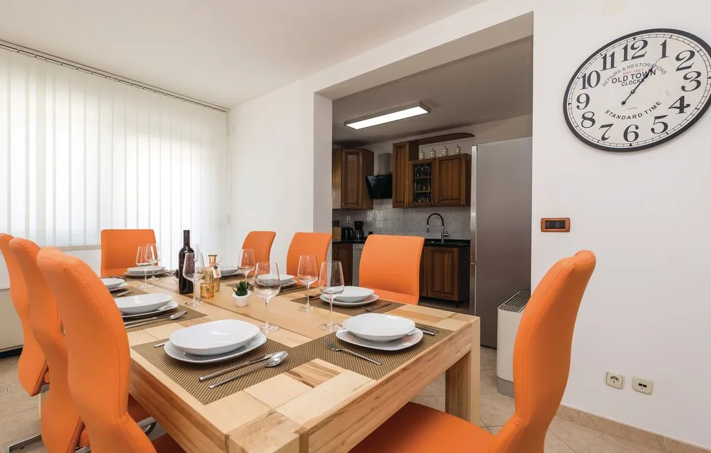 A dining area with a set table and orange seating, opening onto a kitchen.