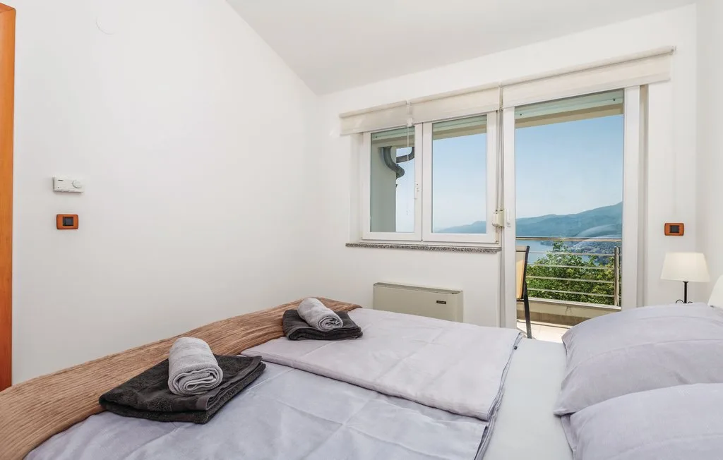 A bright bedroom with beds beside a large window overlooking the water.