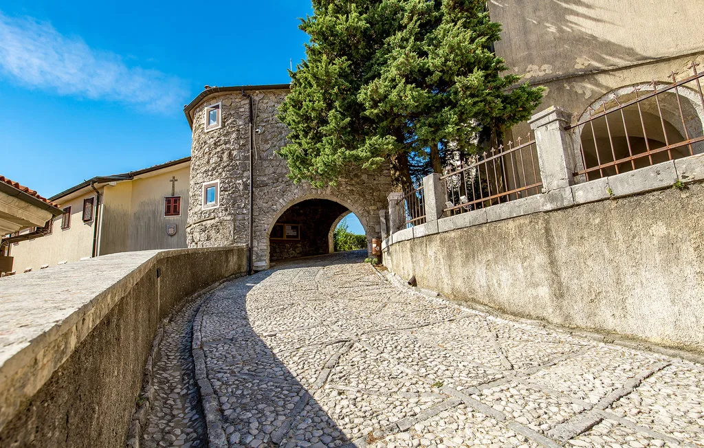 A cobblestone lane curves beneath a stone archway, with trees beside the buildings.