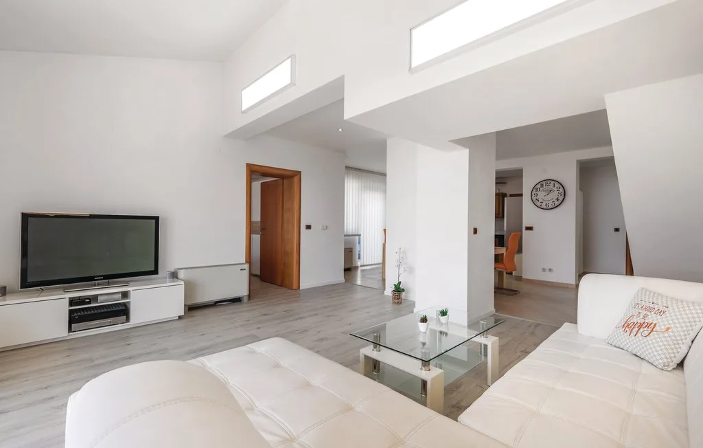 A bright living room with white seating, a glass coffee table, and a television.