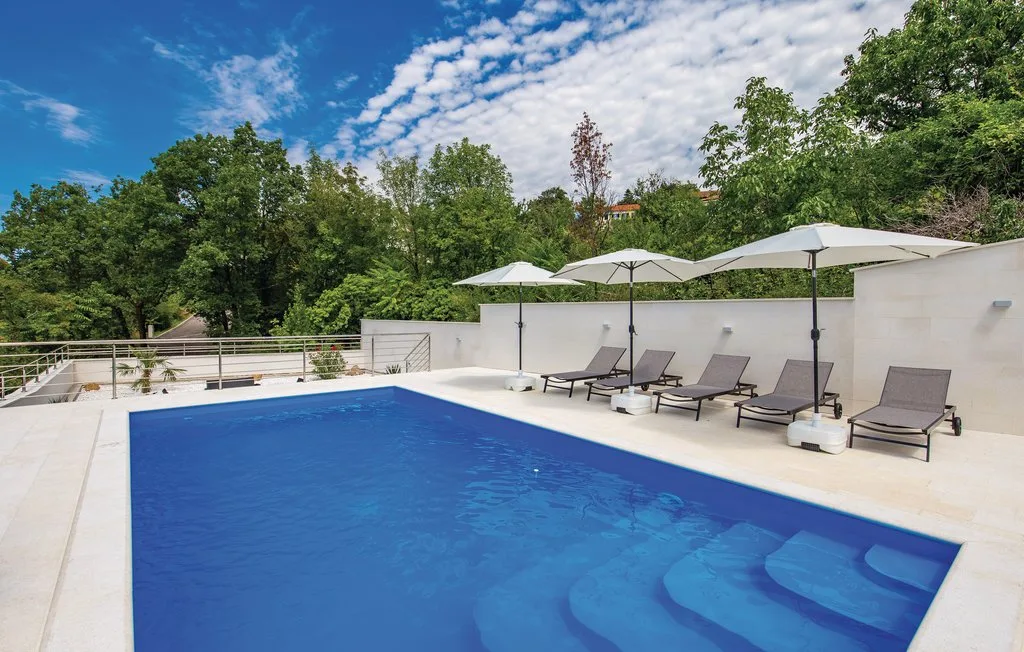 An outdoor swimming pool with lounge seating and umbrellas beside it.