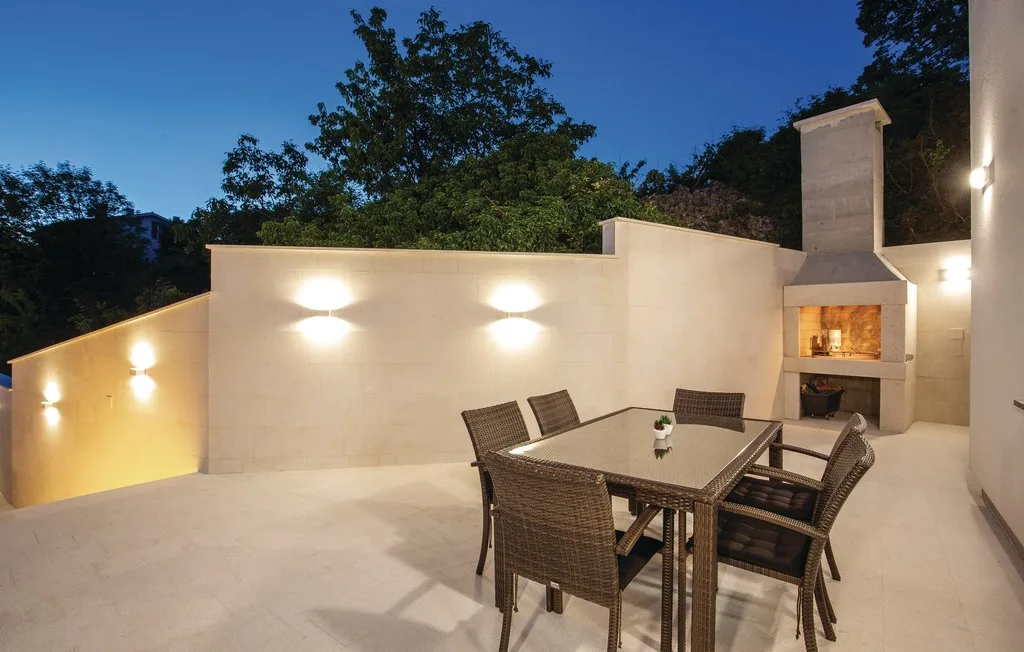 An outdoor dining area with a table and chairs beside a lit fireplace.