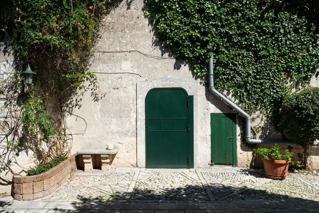 Un patio de piedra con puertas verdes y hiedra trepadora.