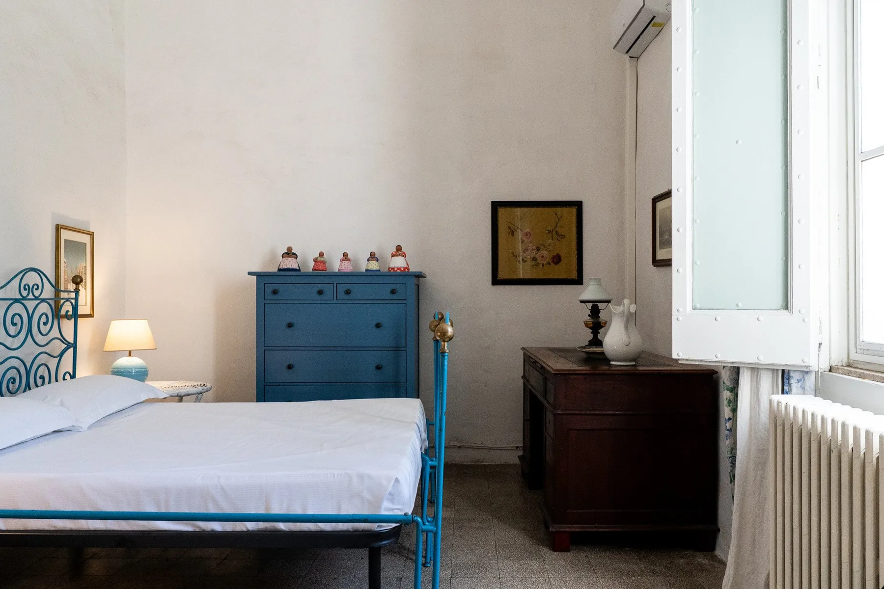Un dormitorio con una cama, una cómoda azul y un escritorio de madera oscura.