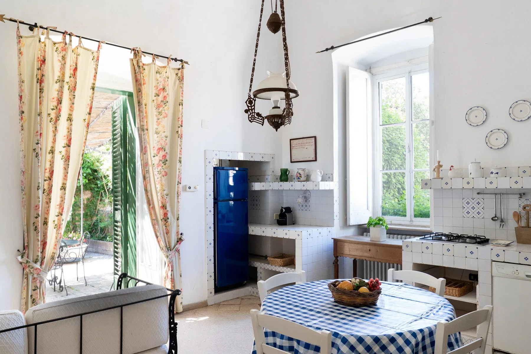 Una cocina luminosa con comedor, refrigerador azul y una mesa junto a la ventana.