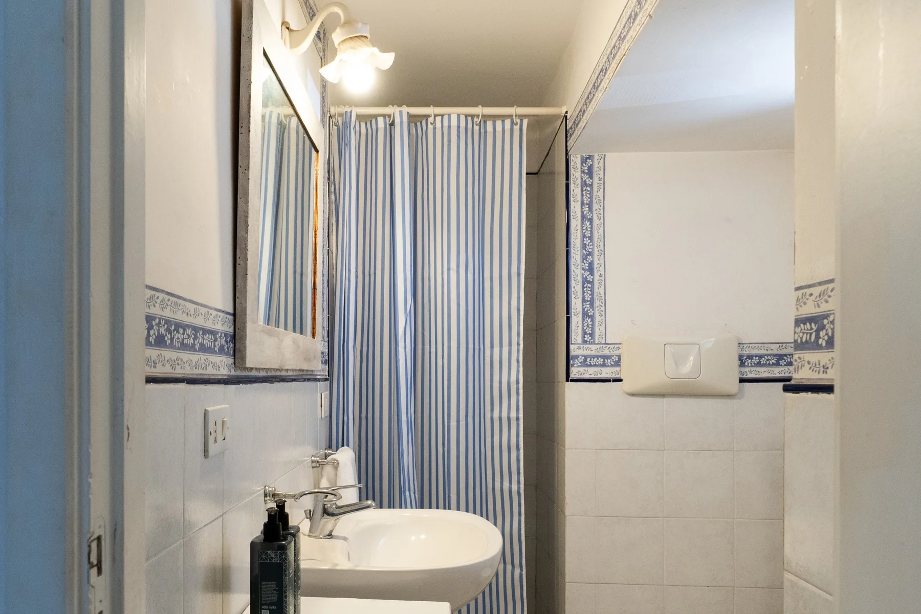 Un baño alicatado con lavabo, espejo y cortina de ducha a rayas.