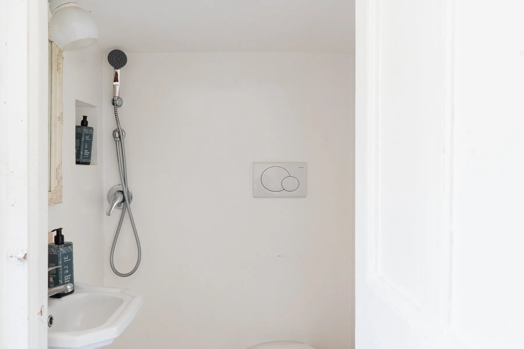 Un baño blanco con ducha de pared y lavabo.