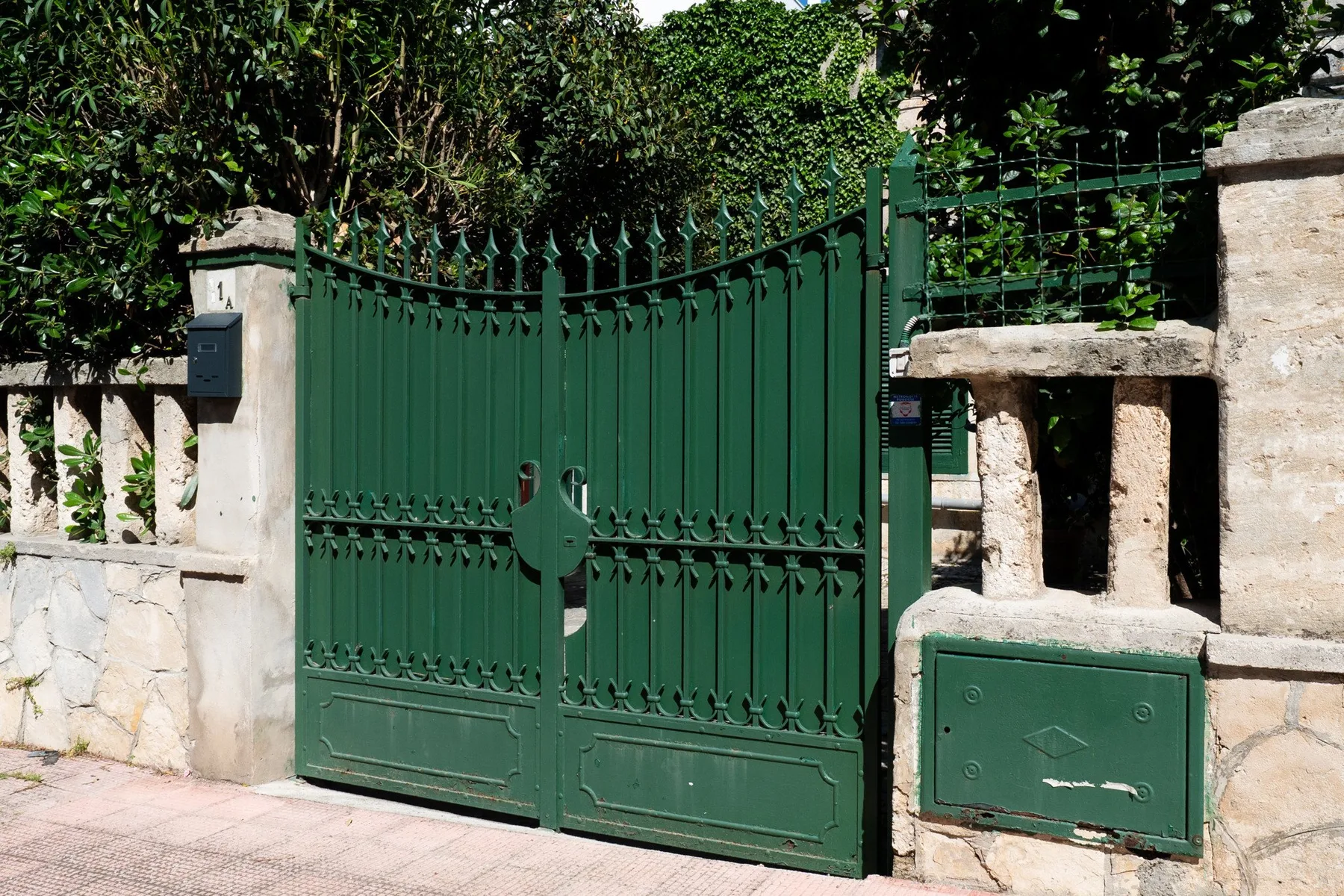 Una puerta metálica verde en un muro de piedra clara.