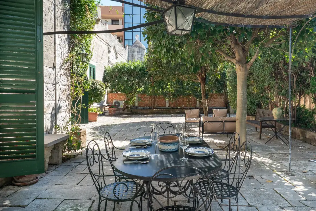 Un patio exterior a la sombra, con una mesa redonda y vegetación alrededor.